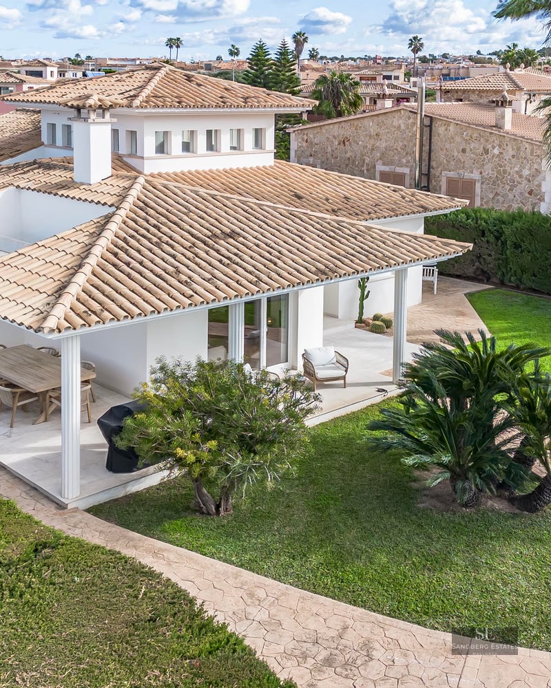 Aerial view of a white Mediterranean villa with terracotta roof, swimming pool, and lush green lawn.