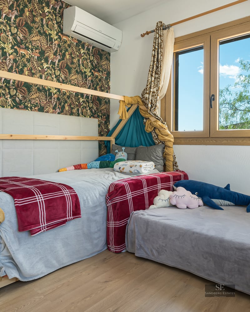 Bright child's bedroom featuring a wooden house bed, jungle wallpaper, and natural light.