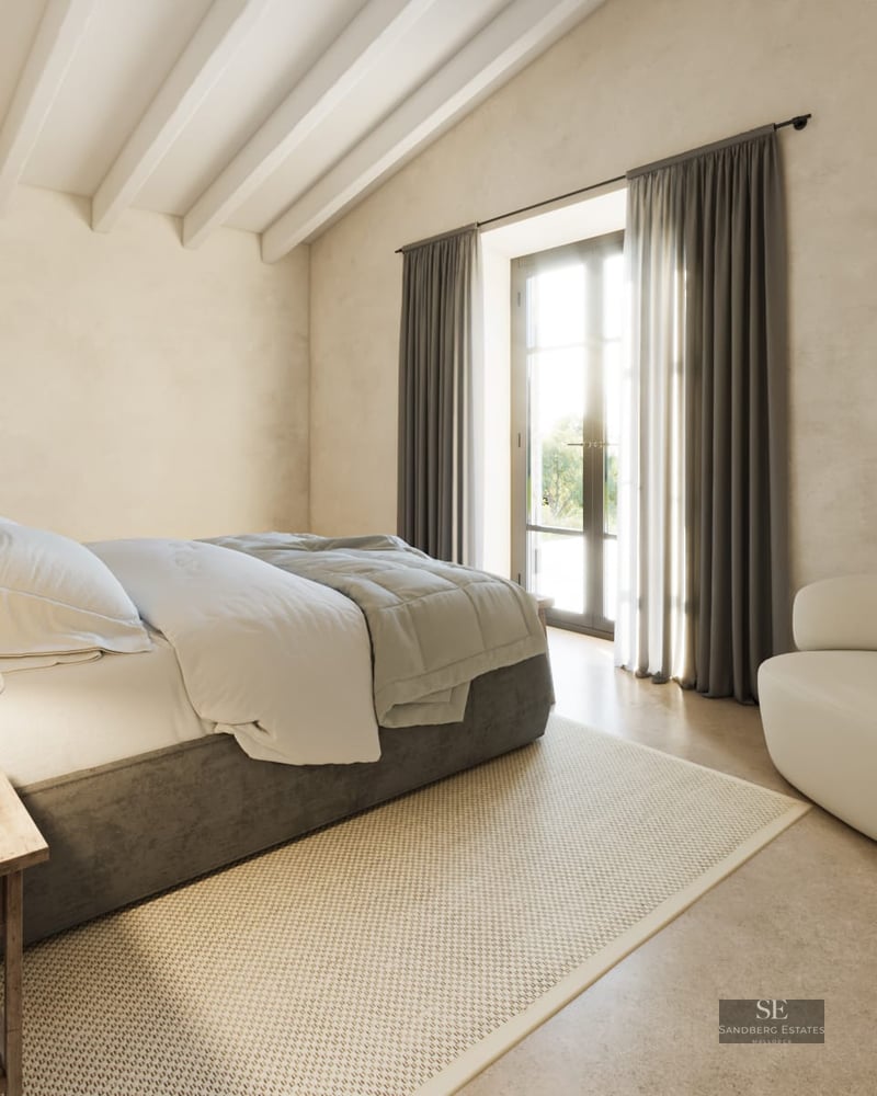 Bright minimalist bedroom with exposed white ceiling beams, a grey bed, white armchair, and glass door to a terrace.