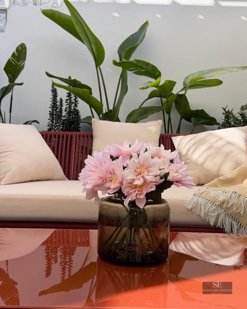 Red rope sofa with cream cushions on a terrace surrounded by tropical plants and a glossy orange coffee table.
