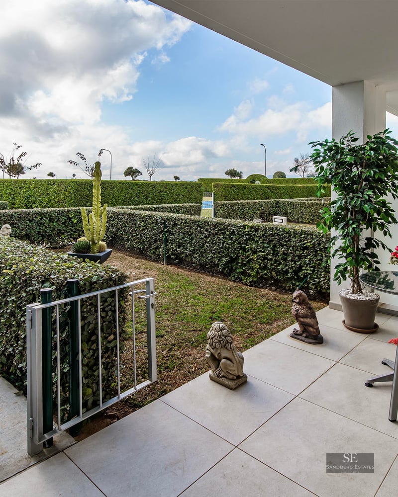 Modern white terrace with two red chairs and table overlooking a private garden with perfectly trimmed hedges.