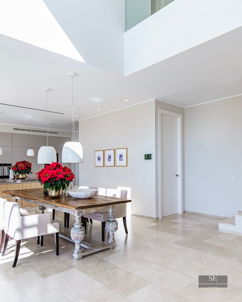 Bright open-concept dining room with a rustic wood table, marble floors, and a modern wooden slat staircase partition.