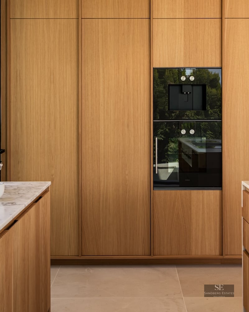 Modern kitchen featuring floor-to-ceiling oak cabinets, white marble countertops, and integrated black appliances.