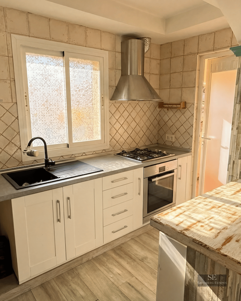 A kitchen featuring white cabinets, a gray countertop, a gas stove, and a rustic wood-finished breakfast bar.