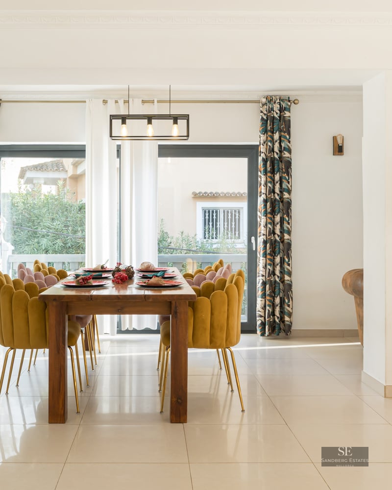 Espace salle à manger moderne avec table en bois, chaises en velours jaune, sapin de Noël et grandes baies vitrées.