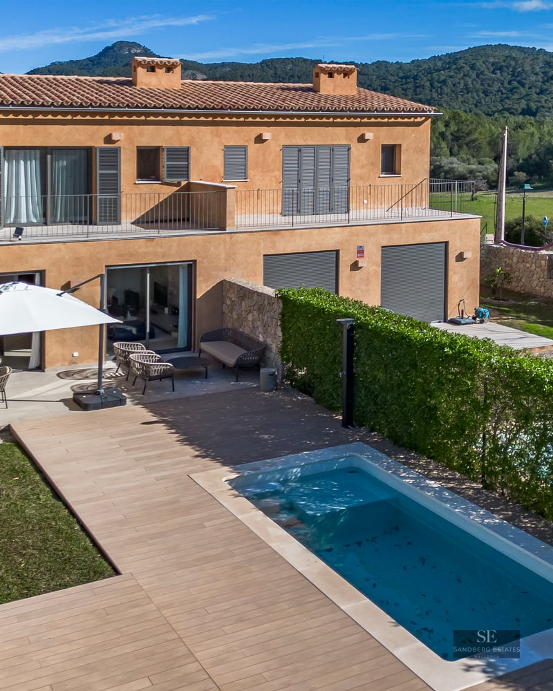 Aerial view of an ochre-colored villa featuring a swimming pool, wooden deck, garden, and hills in the background.