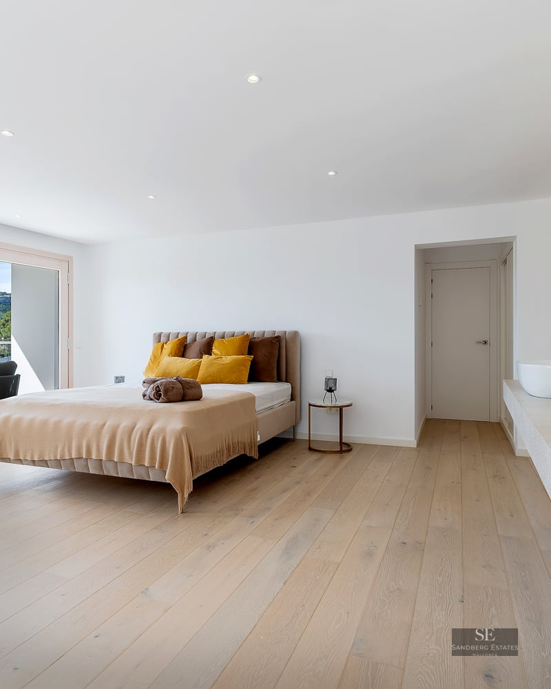 Spacious modern bedroom featuring a bed with yellow pillows, double sinks, and glass doors opening to a scenic mountain view.