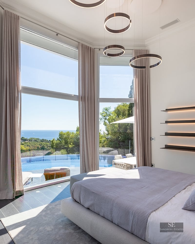 Modern master bedroom with floor-to-ceiling windows overlooking an infinity pool and the Mediterranean sea.