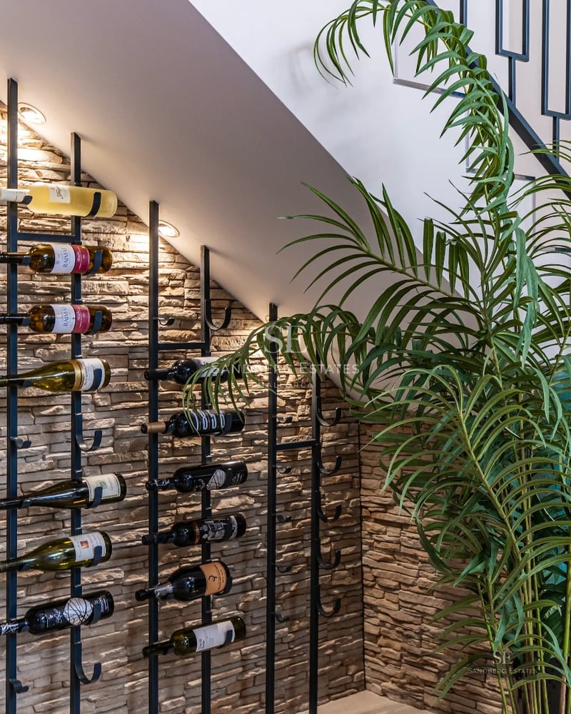 View of infinity pool with sun deck, lounge chairs, and palm trees. Modern architecture, large windows. Natural lighting.