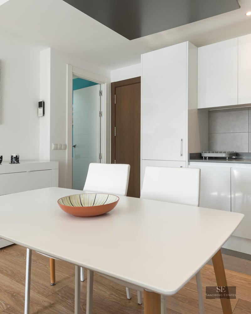 Cuisine moderne lumineuse avec des placards blancs, une crédence grise et une table à manger blanche.