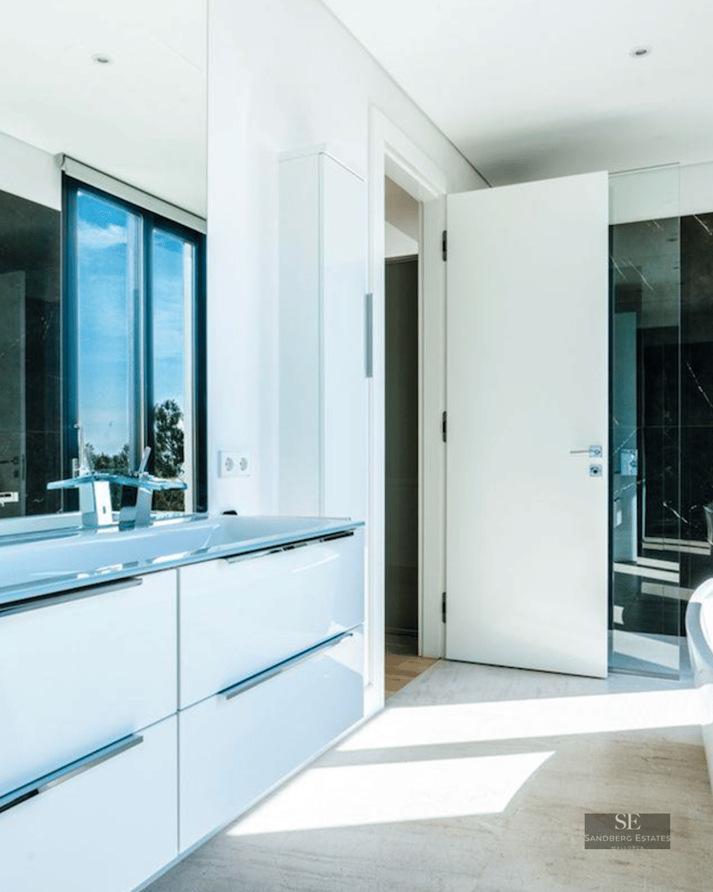 Modern bathroom with white freestanding tub, double vanity, and black marble wall overlooking the sea.