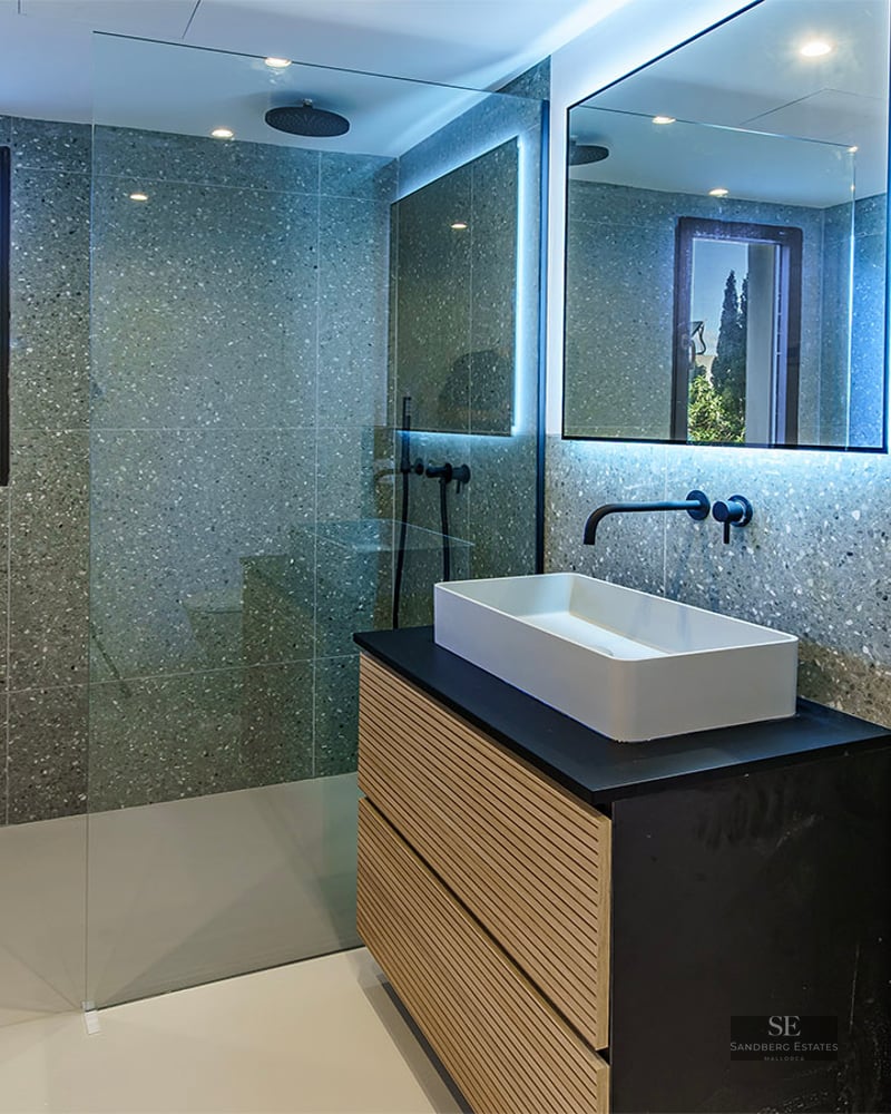Modern bathroom with grey terrazzo walls, a walk-in glass shower, black fixtures, and a wooden vanity with a white sink.