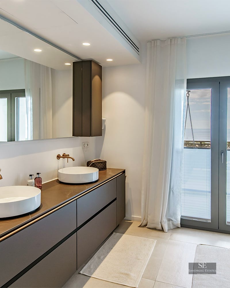 Modern master bathroom featuring a double vanity with vessel sinks, large mirror, and balcony access with sea views.