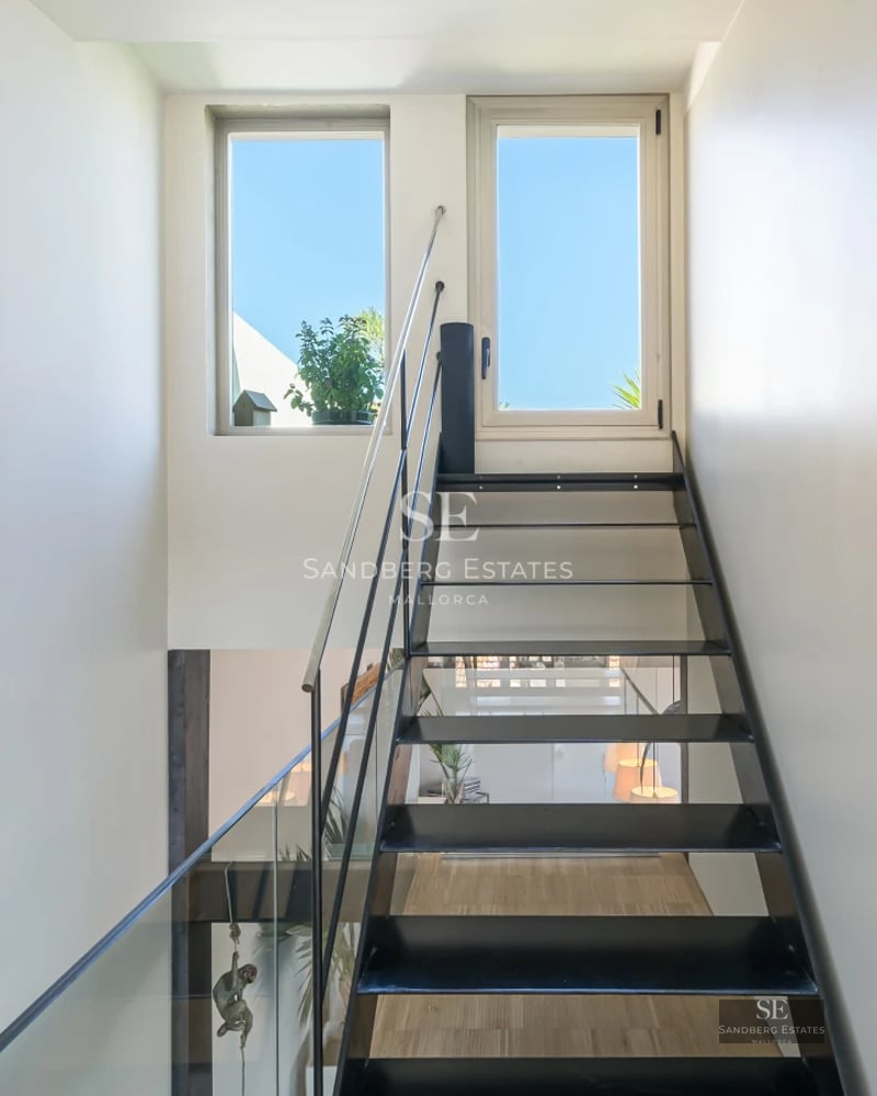 Spacious living room with panoramic windows, light wood floors, modern furniture, and abundant natural light. View of garden and pool.