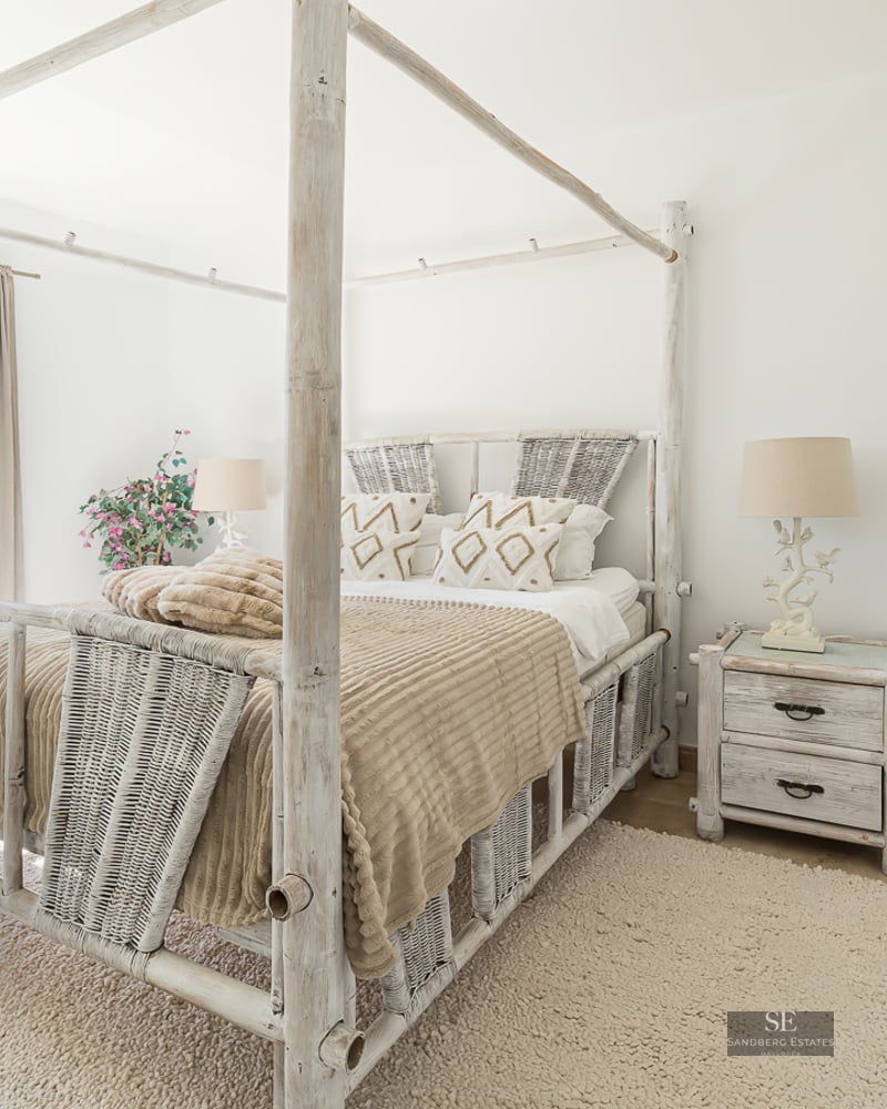 Bright bedroom featuring a white bamboo canopy bed, woven textures, and direct garden access via glass doors.