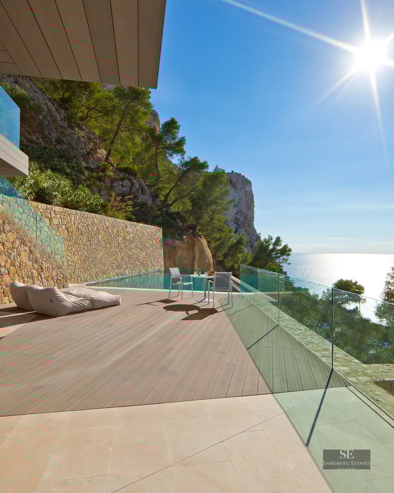 Modern villa terrace with infinity pool, wooden decking, glass railings, and panoramic views of the Mediterranean Sea.