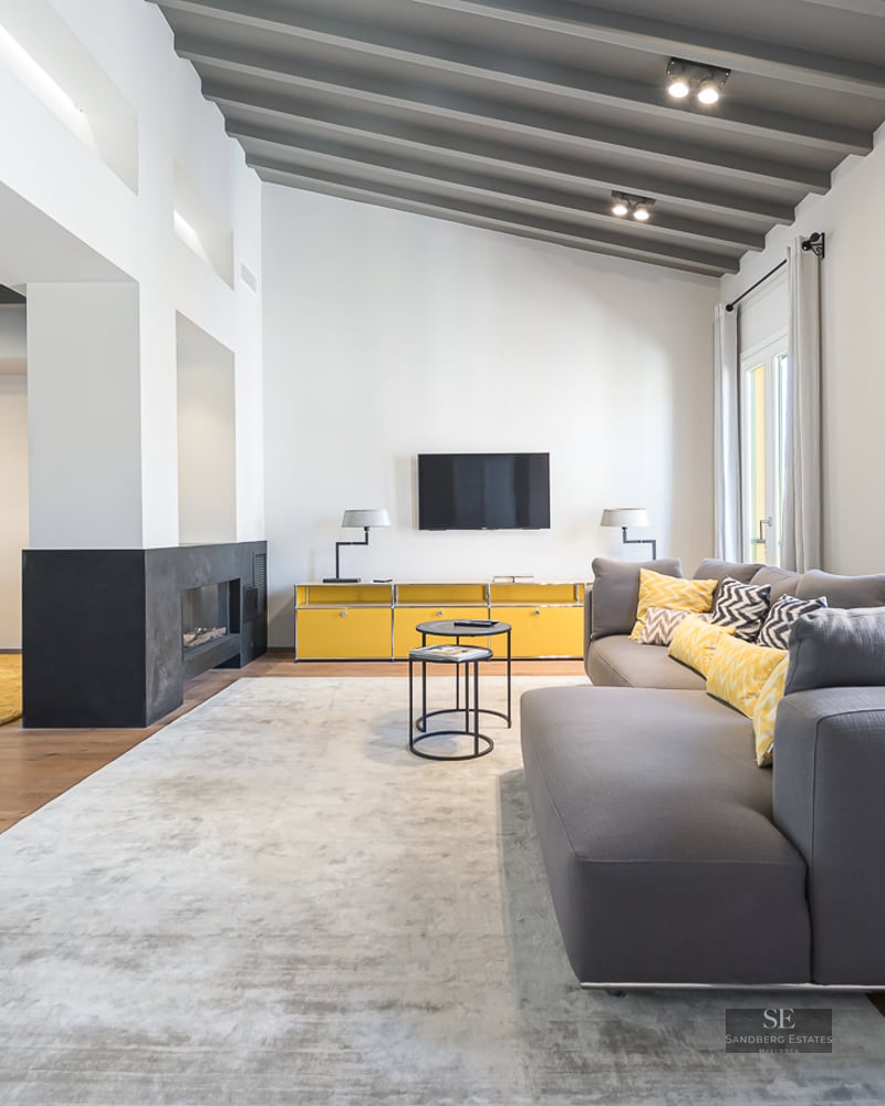 Spacious living room with grey sofa, yellow furniture, fireplace, and exposed beam ceiling.