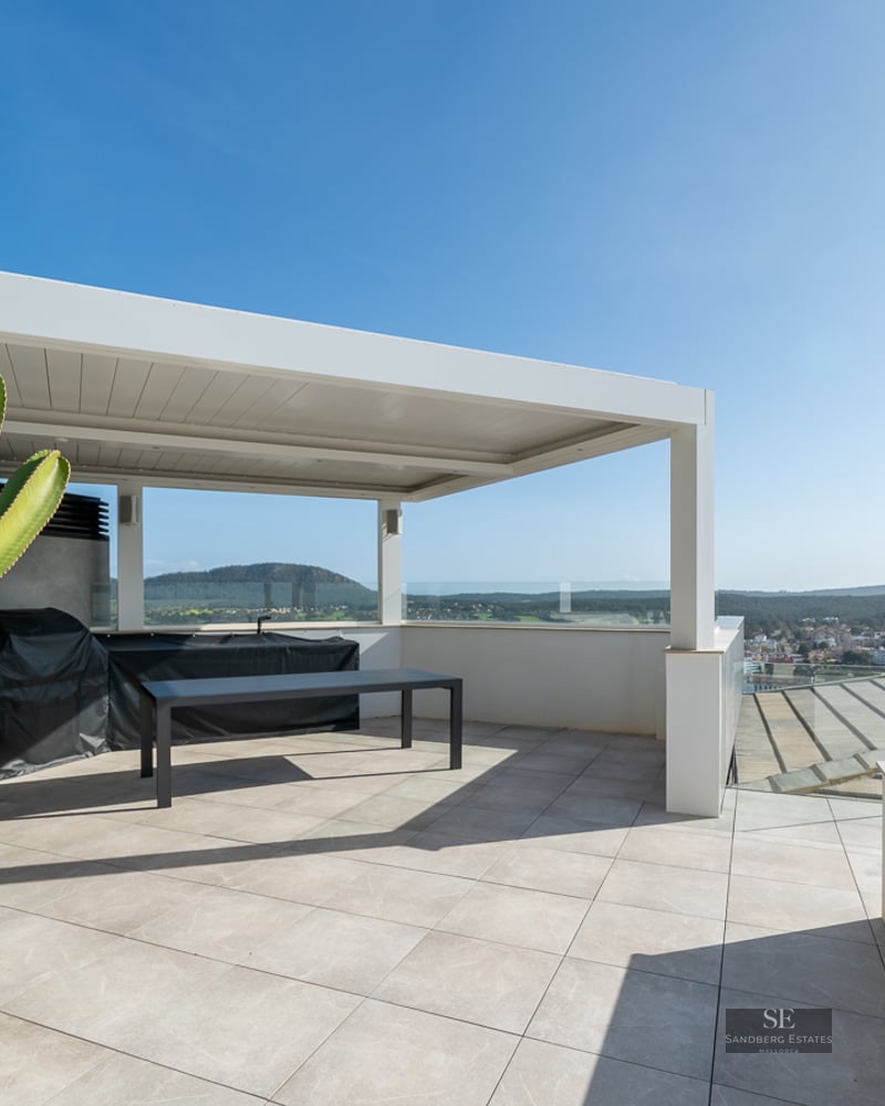 Modern rooftop terrace with a white pergola, outdoor kitchen, large cactus, and scenic views under a clear sky.
