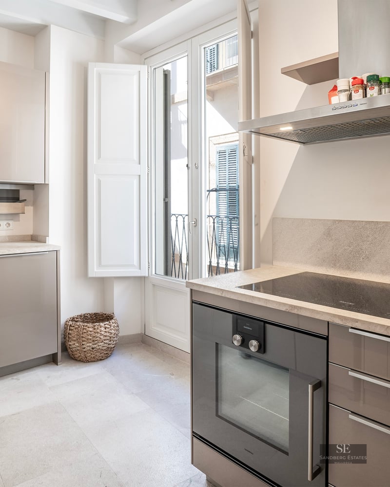 Bright modern kitchen with taupe glossy cabinets, stone countertops, integrated oven, and a balcony door.