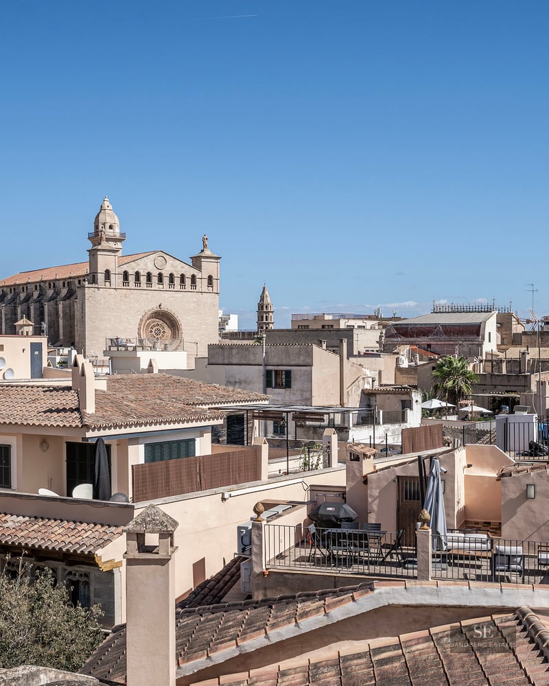 Vue surélevée de toits traditionnels en terre cuite et d'une majestueuse cathédrale en pierre sous un ciel bleu clair.