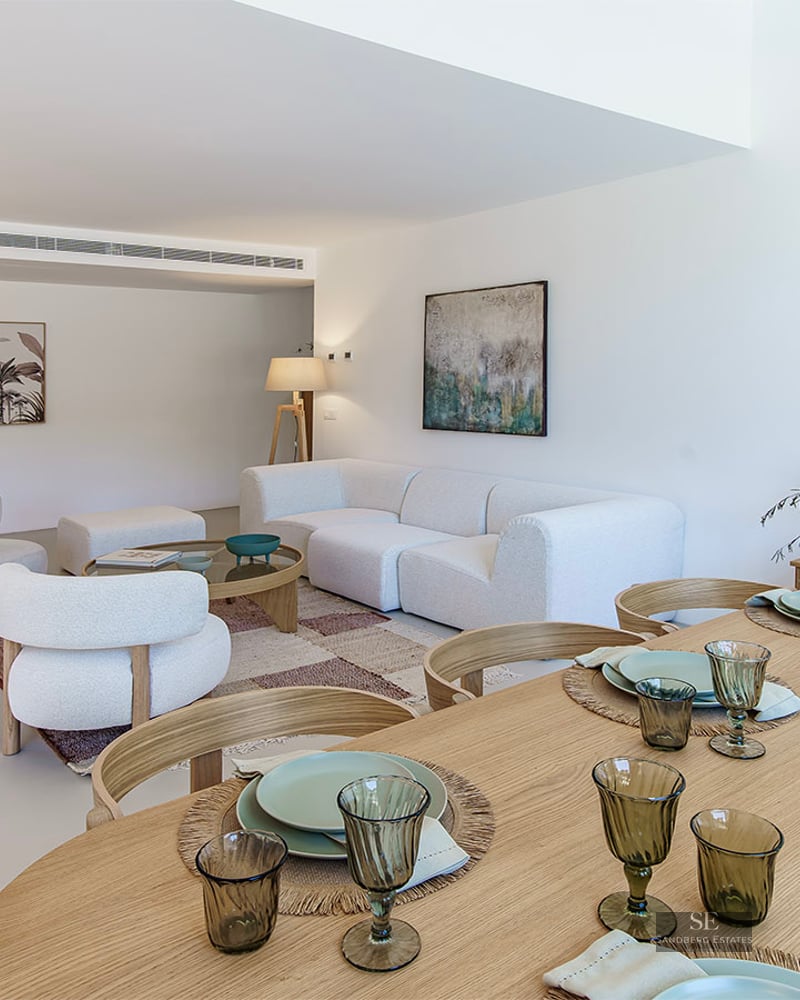 Spacious living and dining area featuring white bouclé sofas, a wooden dining table, and minimalist decor.