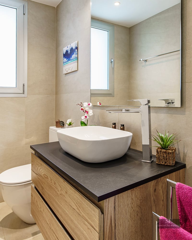 Modern bathroom featuring a white vessel sink on a wood vanity, a large mirror, and beige tiled walls.