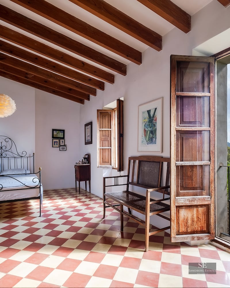 Bedroom featuring a checkered floor, wrought iron bed, wood-beamed ceiling, and an open door viewing lush mountains.