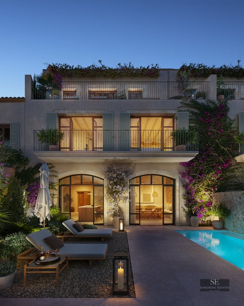 Luxury outdoor patio with a glowing blue pool, sun loungers, stone walls, and a Mediterranean villa at night.