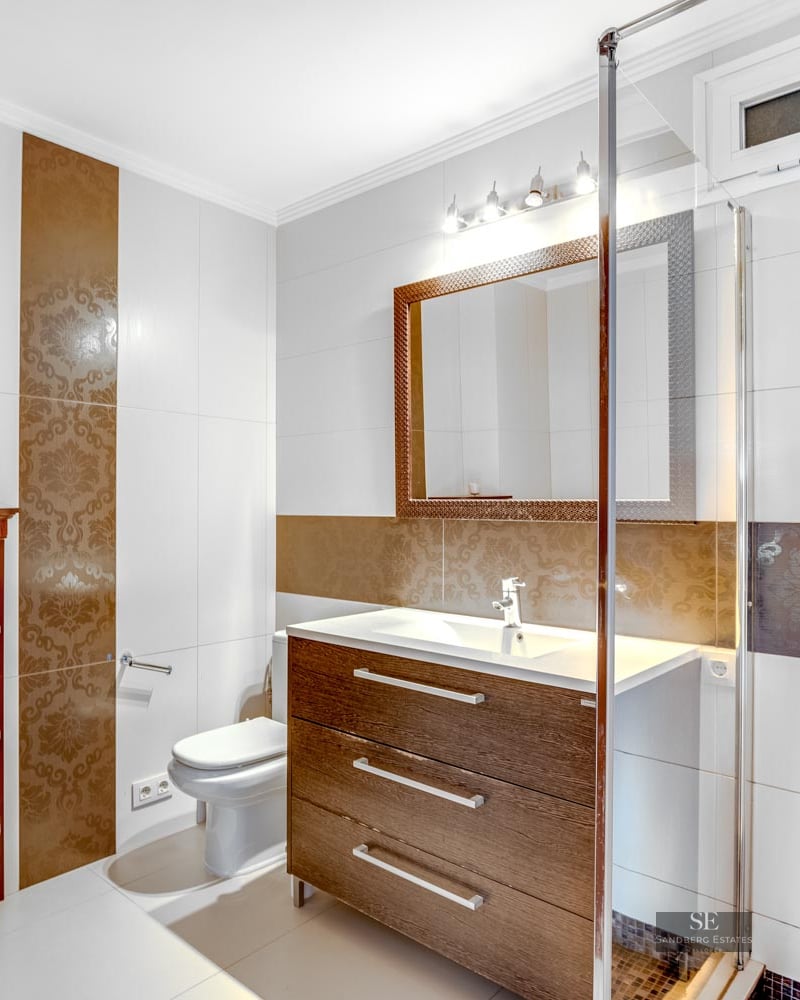 Modern bathroom with dark wood vanity, glass shower enclosure, and decorative patterned tiles.