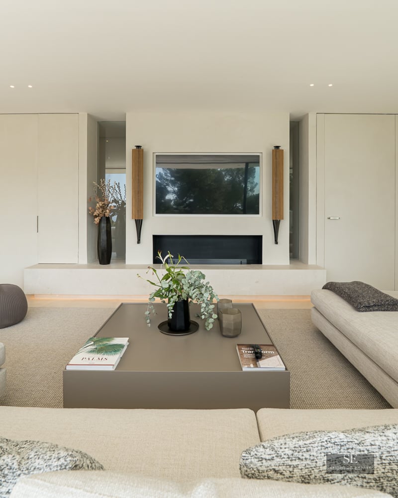 Spacious living room featuring beige sofas, an integrated fireplace, and a modern coffee table in neutral tones.