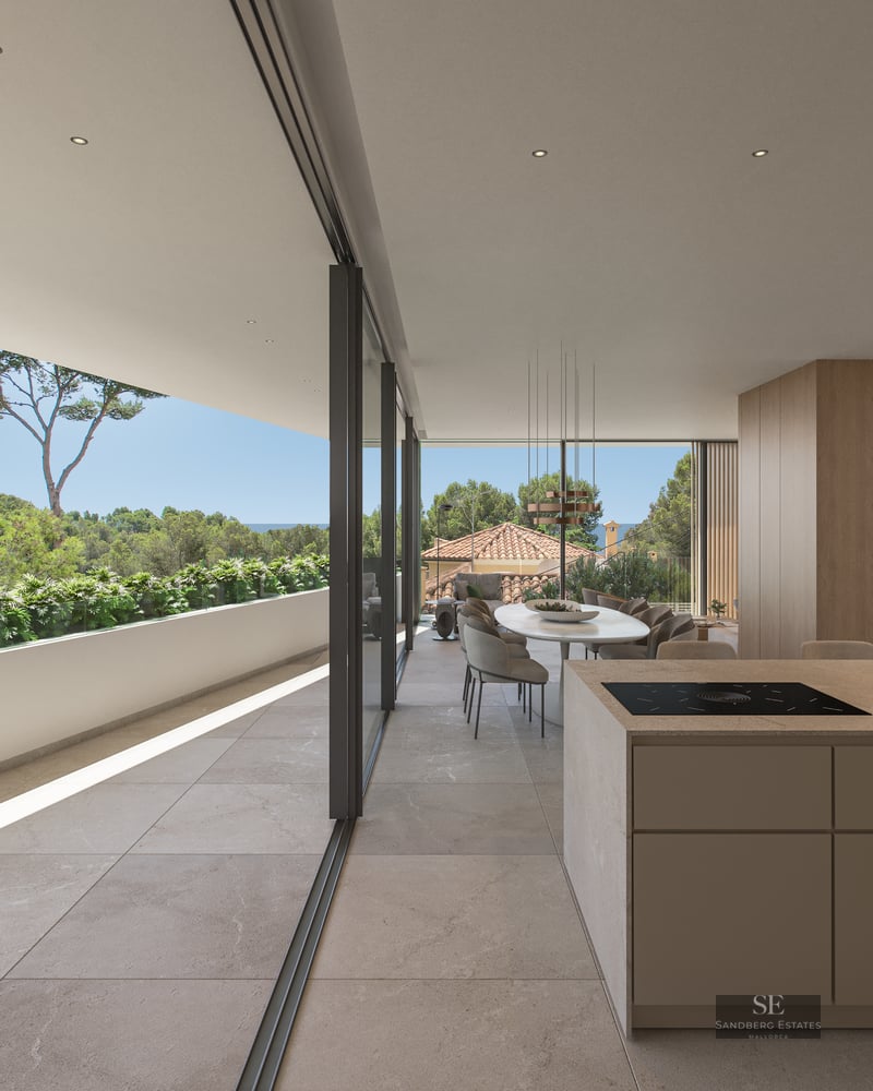 Modern open-plan dining room with stone floors, kitchen island, and glass doors opening to a lush terrace and sea view.