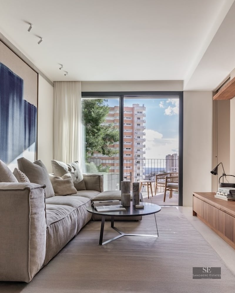 Bright modern living room featuring a plush beige sofa, abstract blue art, wooden TV console, and a balcony view.