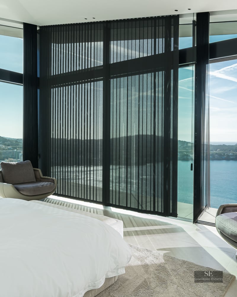 Modern bedroom with floor-to-ceiling windows offering a panoramic sea view and designer swivel chairs.