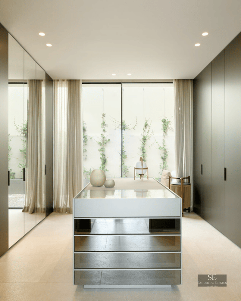 Modern walk-in closet with dark floor-to-ceiling cabinets, a mirrored island, and a garden window.
