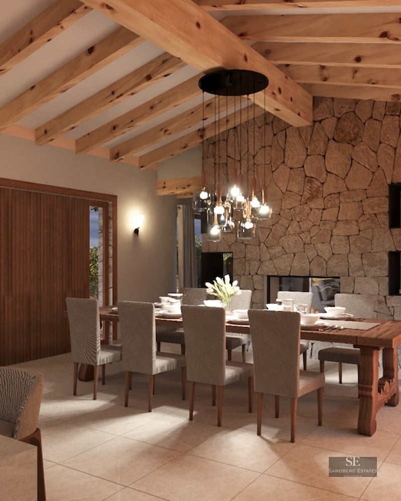 Interior view of a luxury dining room with high wooden beam ceilings, a natural stone feature wall, and a large dining table.