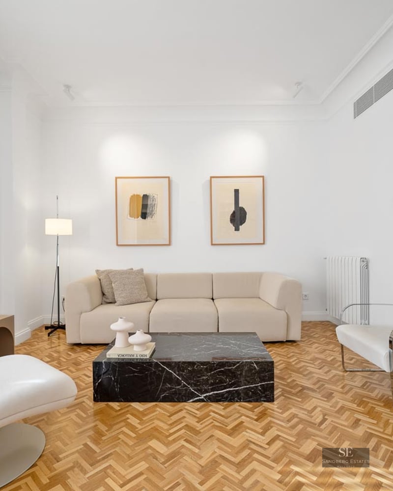 Bright living room with white walls, herringbone wood floor, beige sofa, and a striking black marble coffee table.