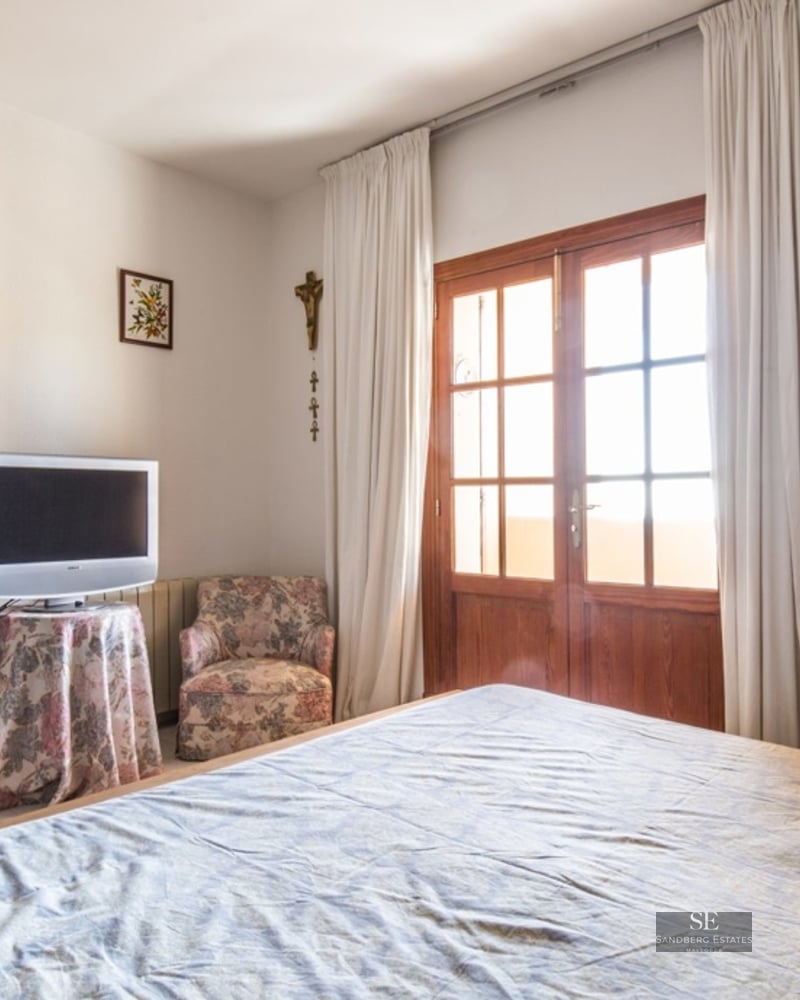Bedroom featuring a bed, two floral armchairs, and wooden French doors leading to a balcony.