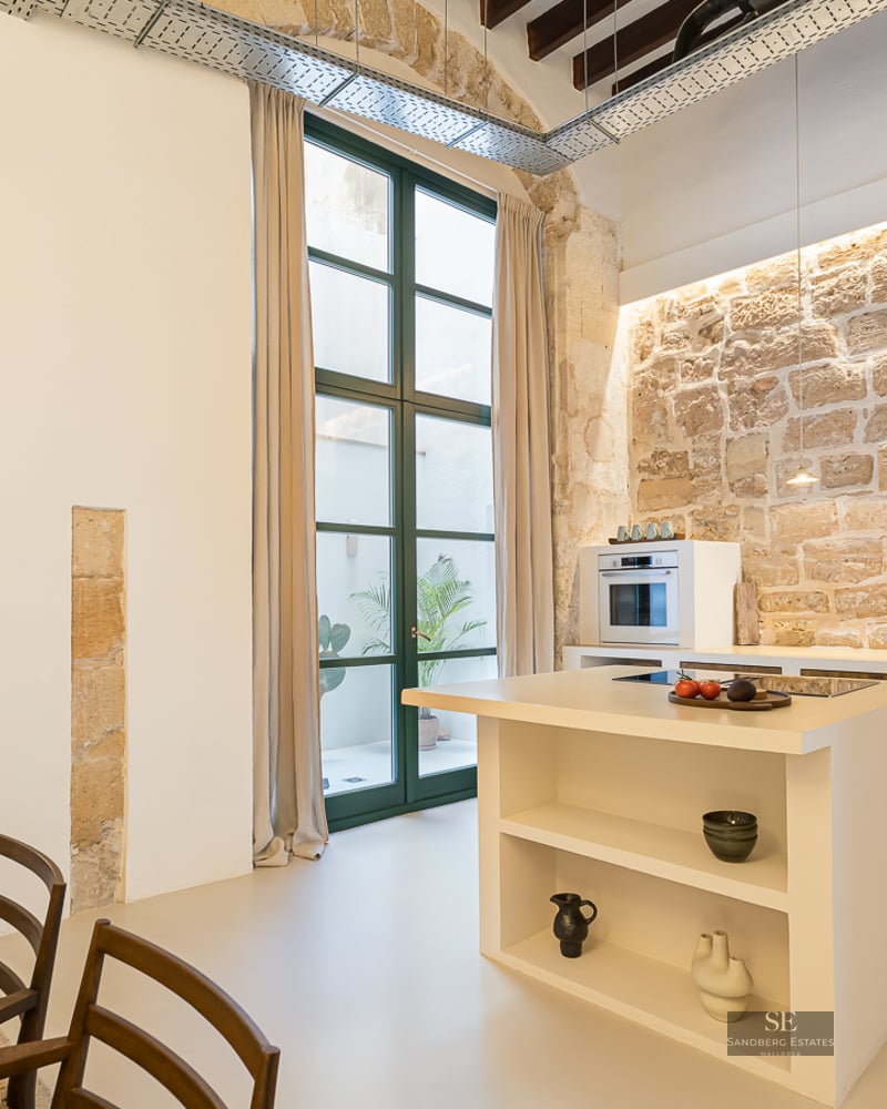 Minimalist kitchen featuring a large natural stone wall, white island, and high ceilings with wooden beams.