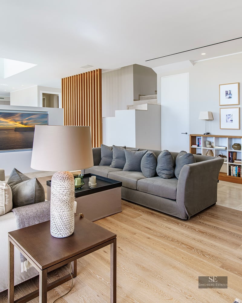 Spacious modern living room with grey sofas, light wood floors, a skylight, and a decorative wooden slat wall.