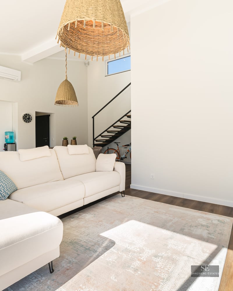 Salon spacieux avec canapé d'angle blanc, luminaires en rotin et parquet foncé.