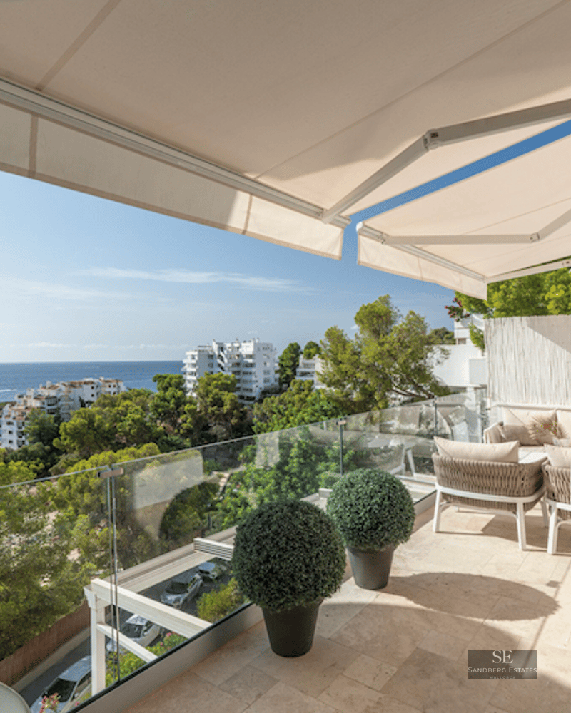 Modern terrace with beige sofas, glass railings, and panoramic Mediterranean sea views under retractable awnings.