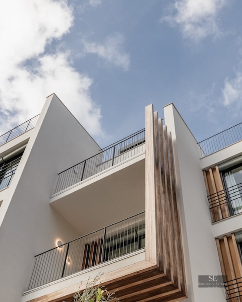 Low-angle view of a modern white building facade with wooden accents and black railings against a blue sky.
