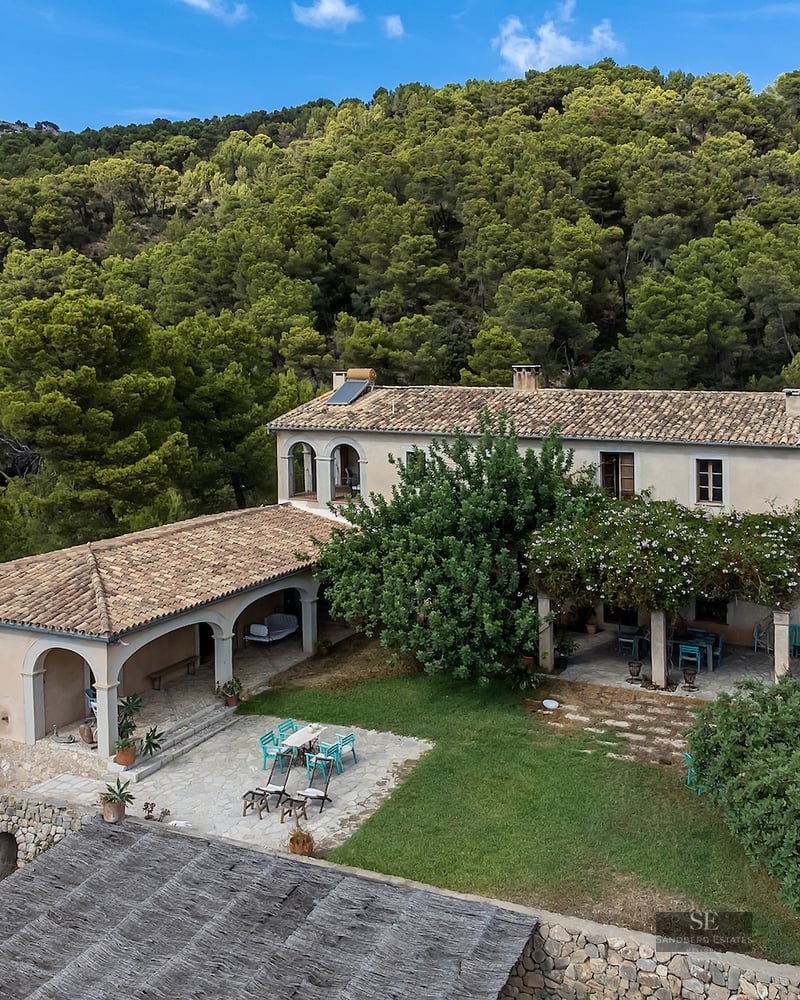 Elevated view of a Mediterranean stone villa with terracotta roof surrounded by a dense pine forest.