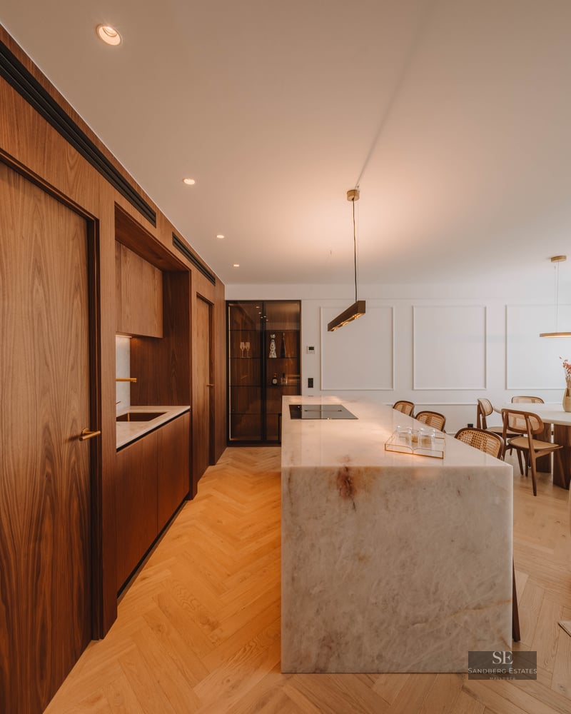 Modern open-plan kitchen featuring a large marble island, walnut cabinetry, and herringbone wood floors.