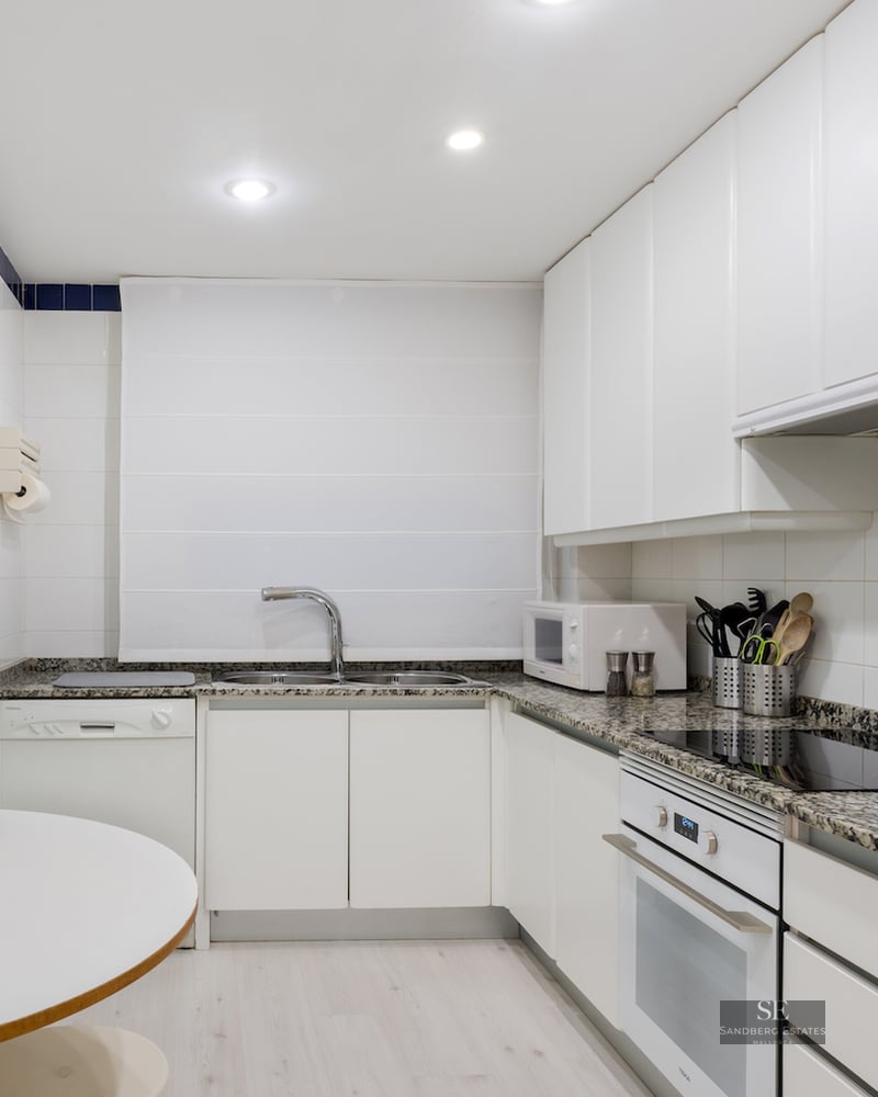 Modern white kitchen with granite countertops, integrated appliances, and a small breakfast table area.