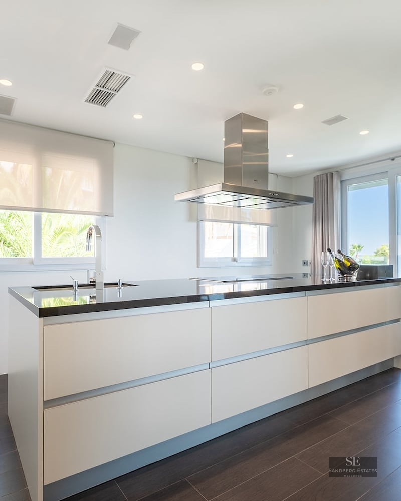 Bright modern kitchen featuring a large white island with black countertop, stainless steel appliances, and sea views.