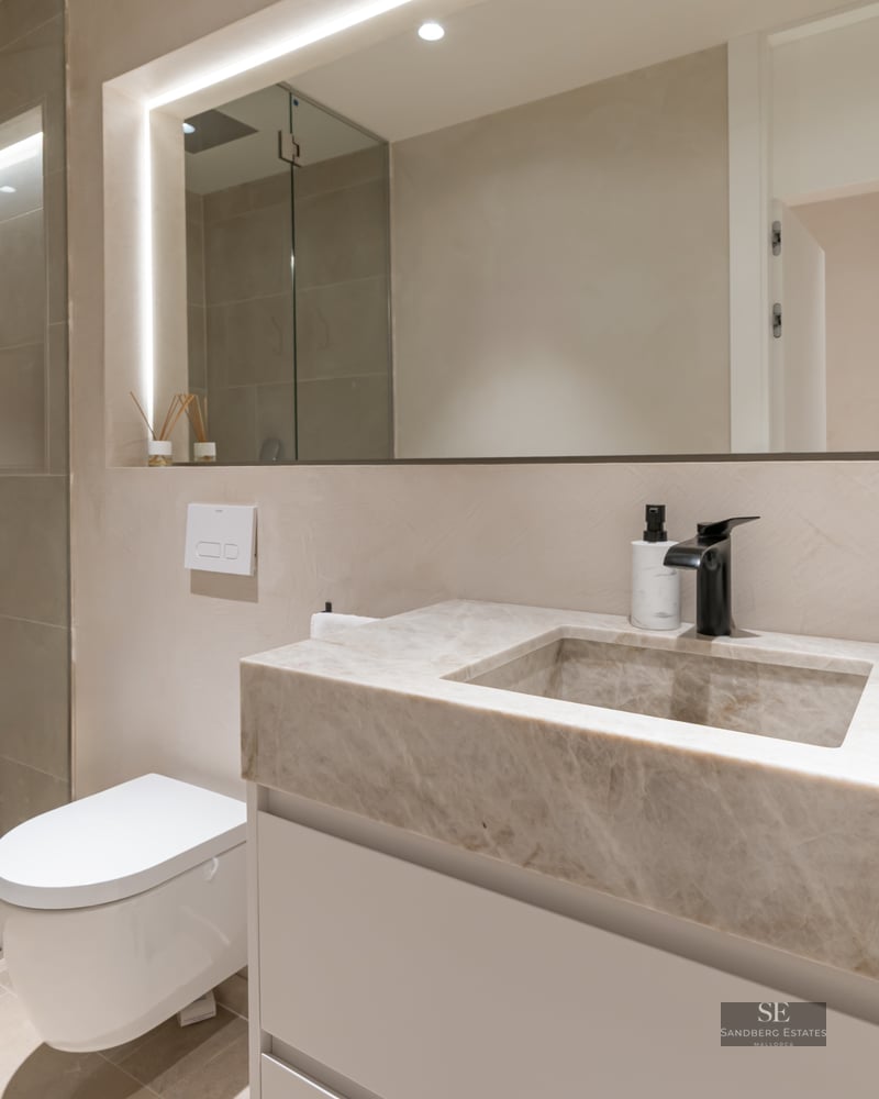 Modern bathroom featuring a stone vanity with integrated sink, black faucet, backlit mirror, and glass walk-in shower.