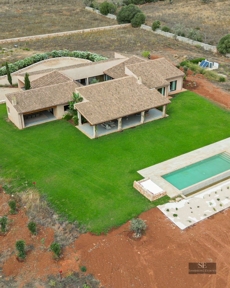 Aerial drone shot of a modern villa with terracotta roof, green lawn, and rectangular pool in the countryside.