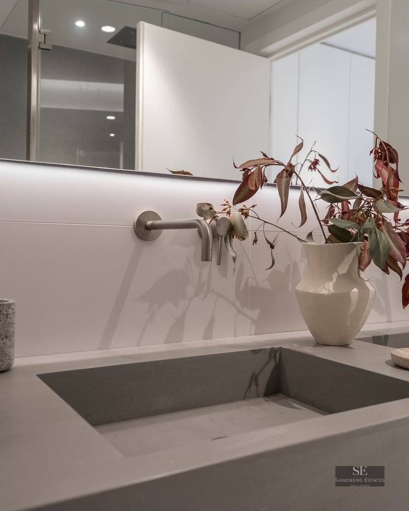 Gray integrated dual sinks with wall-mounted faucets and a large backlit mirror in a modern bathroom.