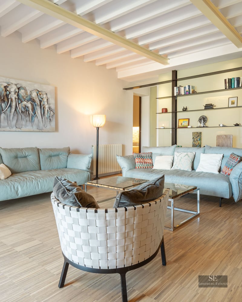Spacious modern living room with light blue sofas, a woven designer armchair, and white exposed ceiling beams.